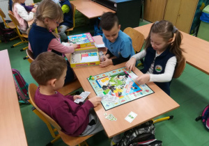 Dwóch chłopców i dwie dziewczynki grają w grę planszową "Monopoly" przy stoliku.