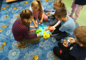Grupa dzieci siedzą w kole na dywanie i grają wspólnie w grę.