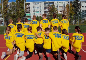 Grupa uczniów obrócona tyłem, ubrana w żółte koszulki z napisem Olimpijska Łódź