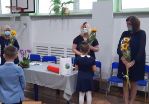 Uczniowie wręczają kwiaty nauczycielom z okazji Dnia Edukacji Narodowej.