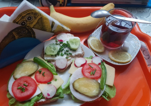Kolorowe kanapki - razowe pieczywo, wędlina, ser żółty, kolorowe warzywne dodatki, banan i herbata z cytryną
