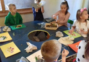 Dzieci siedzą przy stolikach i wykonują prace z papieru czerpanego