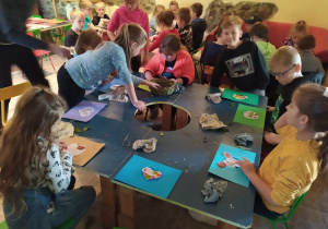 Dzieci siedzą przy stoliku i ozdabiają prace liśćmi