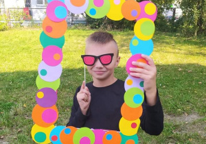 Chłopiec trzymający kolorową ramkę i śmieszne okulary