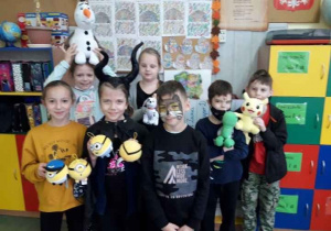 Grupa dzieci w baśniowych strojach pozują do zdjęcia, w rękach trzymają pluszowe zabawki: Olafa, Pikachu, Minionki i inne maskotki.