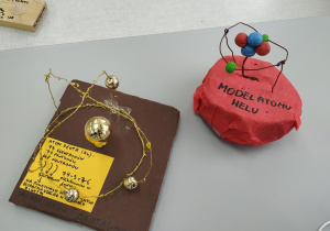 Model atomu helu wykonany z plasteliny i bibuły oraz model atomu złota wykonany ze złotych elementów