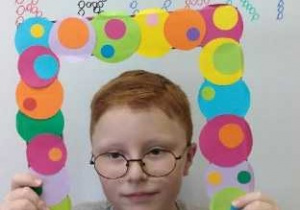 Chłopiec trzymający kolorową ramkę na tle napisu Dzień Kropki