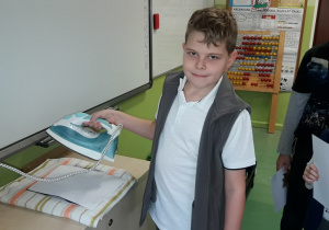 Uczeń trzyma żelazko gotowe do prasowania przygotowanej pracy.