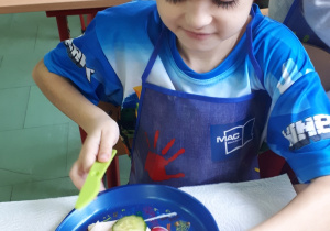 Chłopiec ubrany w fartuszek kroi składniki na kanapkę.