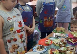 Grupa uczniów w fartuszkach prezentuje przygotowane kanapki.