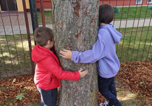 Dzieci przytulają się do drzewa.