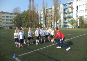 Uczniowie wraz z nauczycielem grają w zbijaka na boisku do piłki nożnej